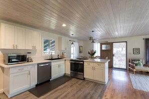 A modern kitchen with white cabinetry, stainless steel appliances, and a wooden floor. - MAUI PAIA HOUSE Walk to beach and charming Paia town! (Paia)