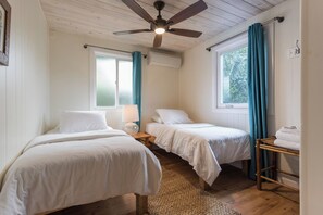 A bedroom with two single beds, a ceiling fan, a window with curtains, and a wooden floor. - MAUI PAIA HOUSE Walk to beach and charming Paia town! (Paia)