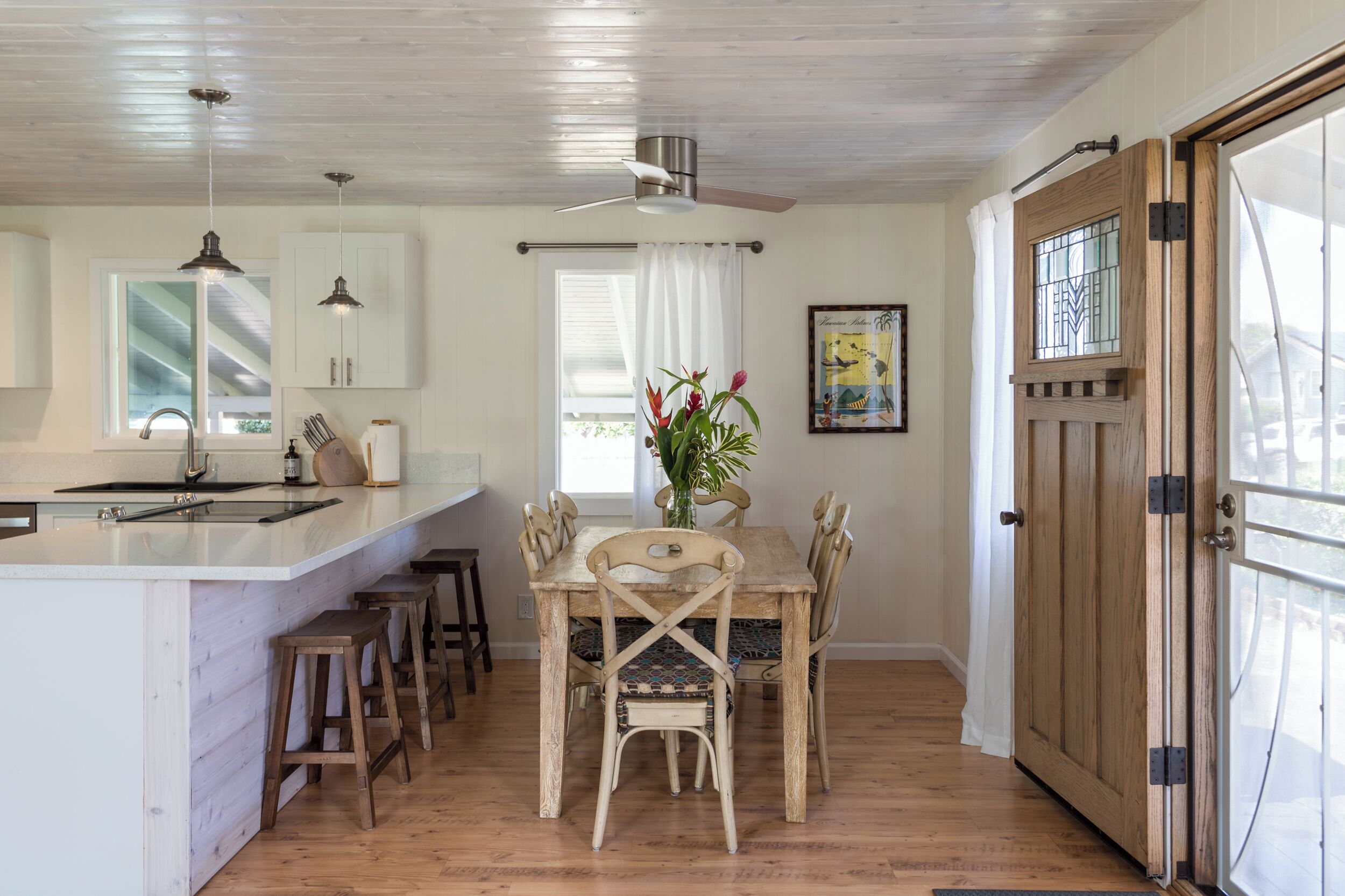 A kitchen with a central island, wooden chairs, a dining table, and a ceiling fan.