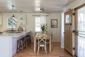 A kitchen with a central island, wooden chairs, a dining table, and a ceiling fan. - MAUI PAIA HOUSE Walk to beach and charming Paia town! (Paia)