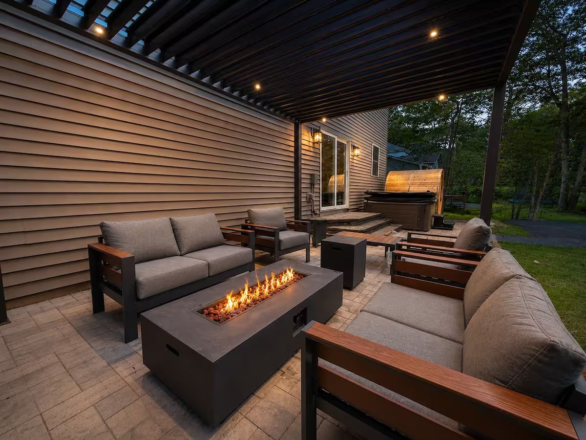 Eine Terrasse im Freien mit Feuerstelle, Sitzgelegenheiten und Blick auf ein Haus.