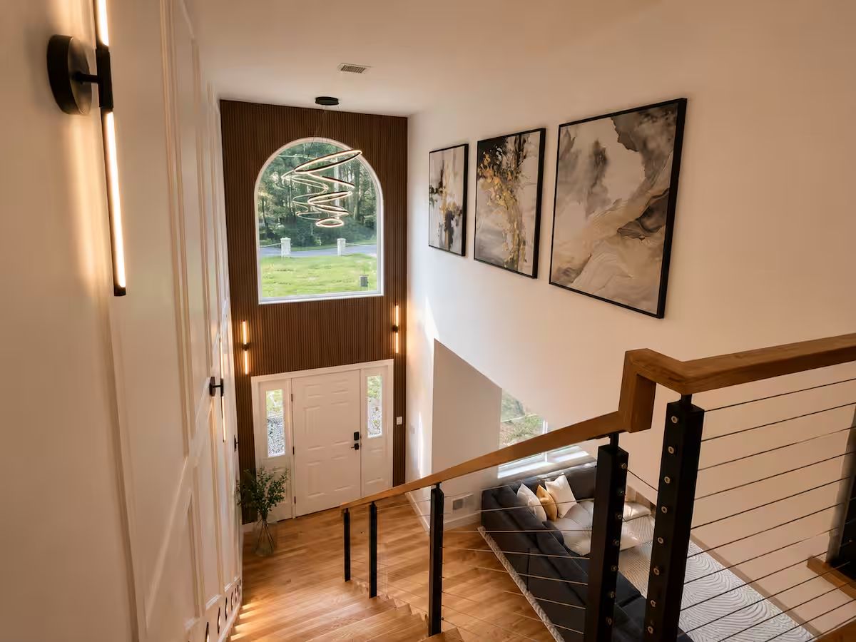Una escalera con barandilla de madera que lleva a un rellano con un sofá y vistas de un jardín.