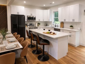 A modern kitchen with white cabinetry, a central island with bar stools, and stainless steel appliances. - New Luxury Stay with Private Pool, Hot Tub, Sauna (Tobyhanna)