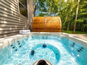 A hot tub with a wooden barrel and a towel beside it, set against a house and trees. - New Luxury Stay with Private Pool, Hot Tub, Sauna (Tobyhanna)