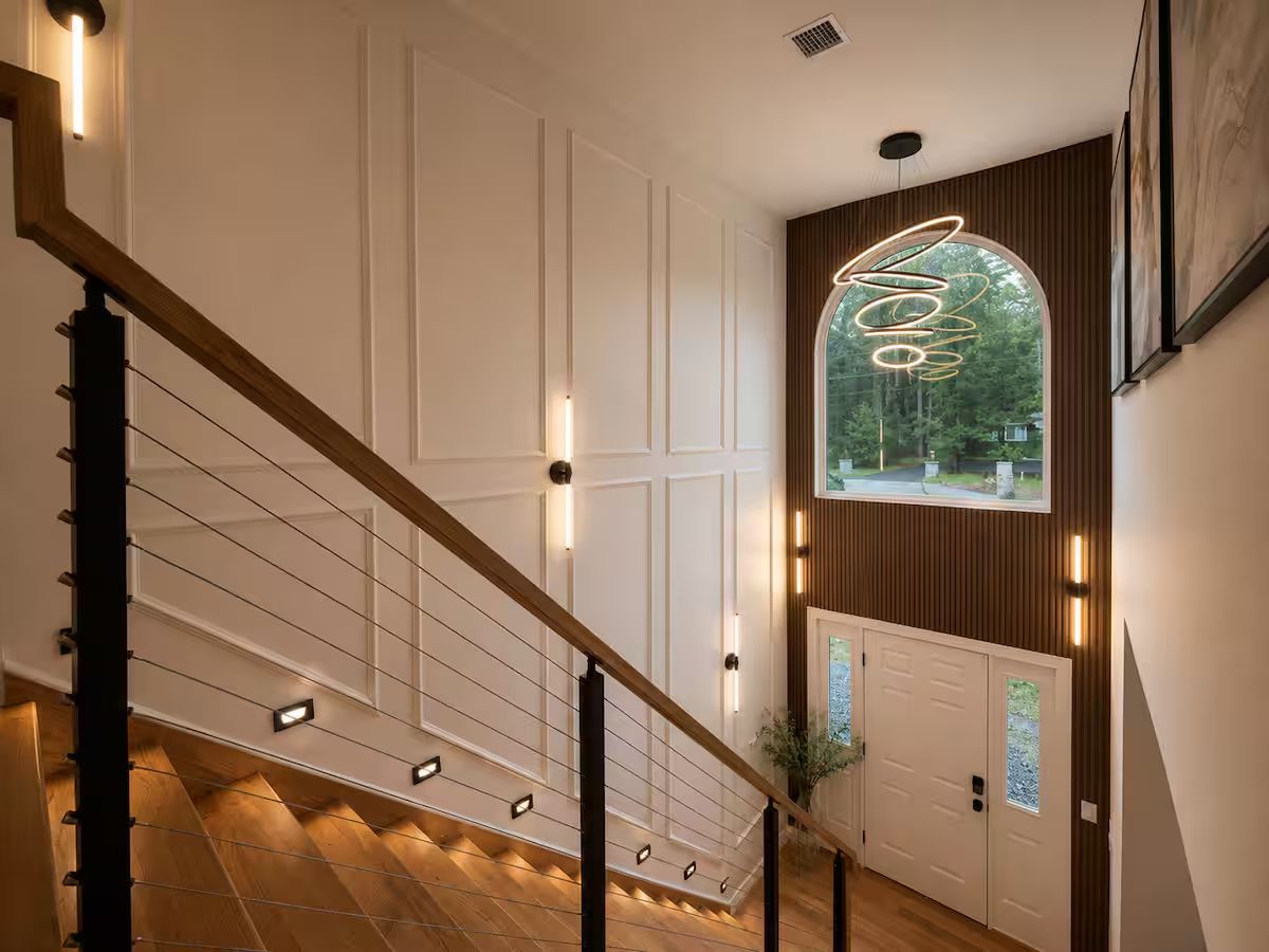 A staircase with a wooden handrail and wall-mounted lights, leading to a door with a frosted glass panel.