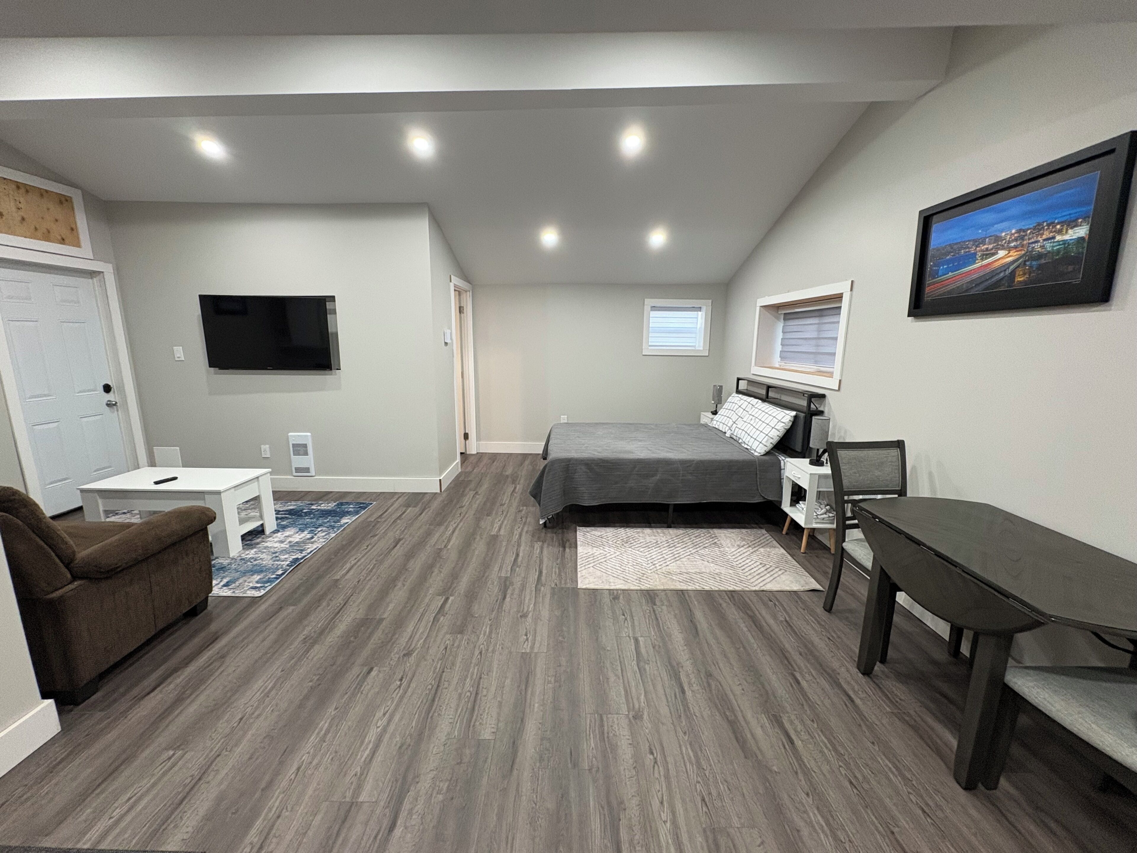 A bedroom with a bed, a desk, a chair, a TV, and a window.