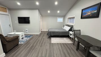 A bedroom with a bed, a desk, a chair, a TV, and a window.
