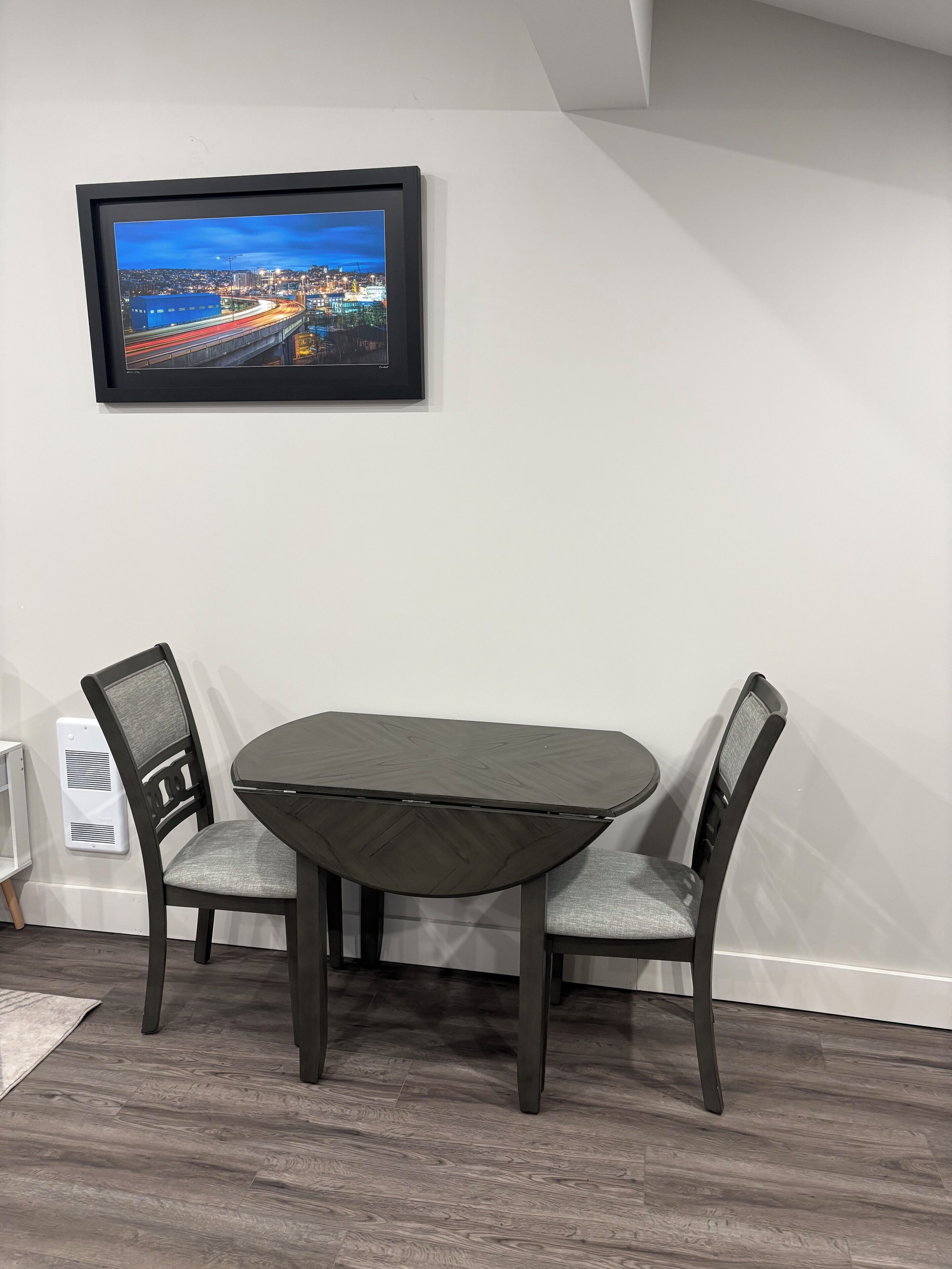A dining area with a table and chairs, a framed picture on the wall, and a white radiator.