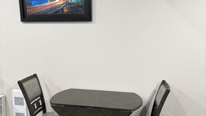 Un coin repas avec une table et des chaises, un tableau encadré au mur et un radiateur blanc.