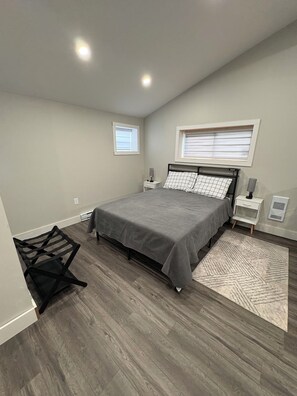 Un dormitorio con una cama, mesitas de noche, una ventana y una silla.