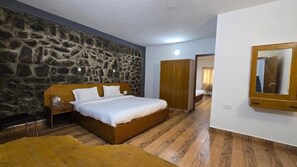 A bedroom with a stone wall, wooden bed, wardrobe, and a mirror. - Vedha Holidays (Kodaikanal)