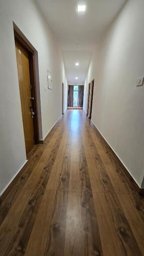 A hallway with wooden flooring and white walls, leading to a door at the end.