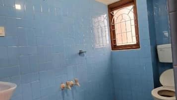 Casa de banho com azulejos azuis, uma pia branca, sanita e janela.