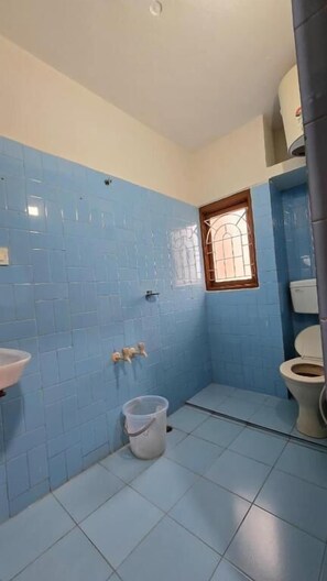 A bathroom with blue tiled walls, a white sink, a toilet, and a window. - Vedha Holidays (Kodaikanal)