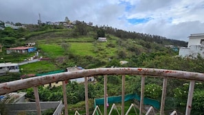 A hillside with a view of a building in the distance, a railing in the foreground, and a green field.