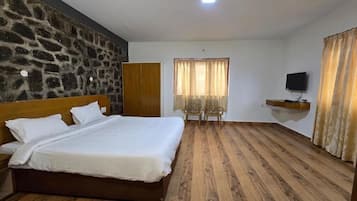 Quarto com uma cama grande, parede de pedra, guarda-roupa de madeira, televisão em uma estante e janela com cortinas.