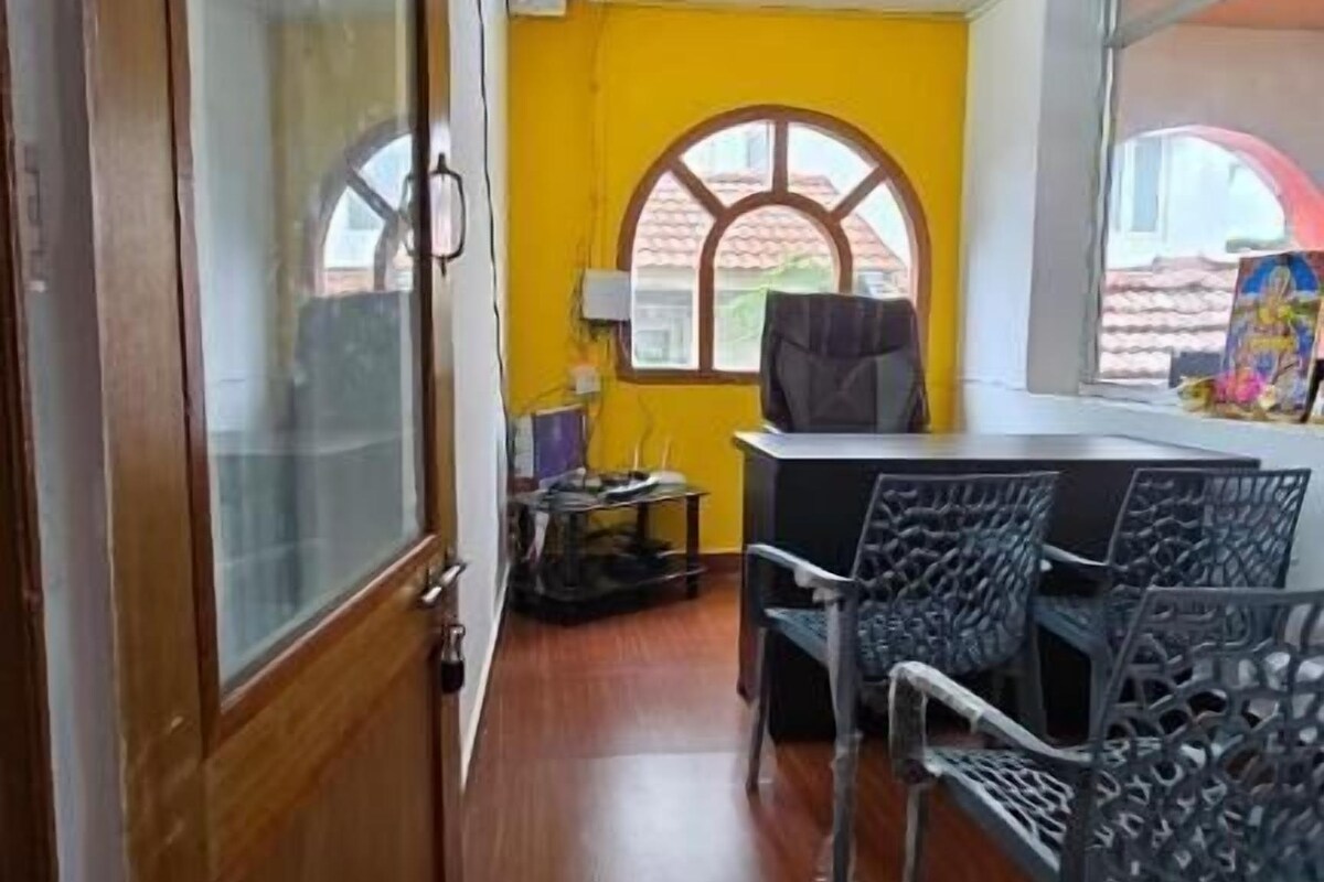A room with a wooden door, a yellow wall, and a window with a view.