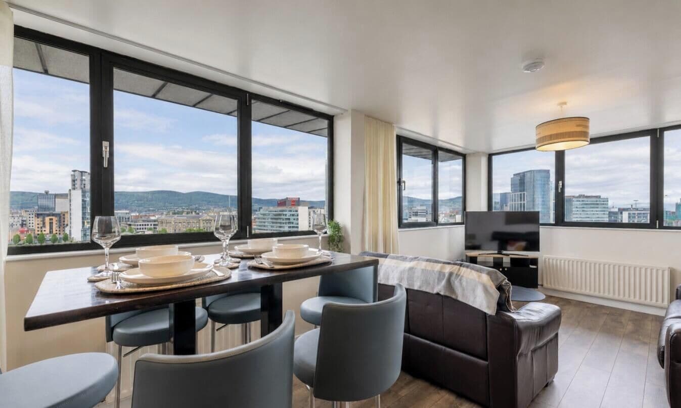 A modern living room with a dining area, large windows, a sofa, and a television.