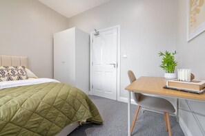Une chambre à coucher avec un lit, un bureau, une chaise, une armoire et une porte.