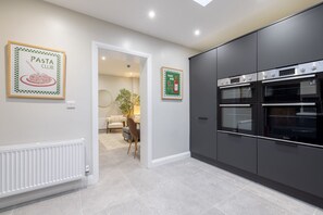 Une cuisine moderne avec des meubles de couleur sombre, un four encastré et un coin repas comprenant une table et des chaises.
