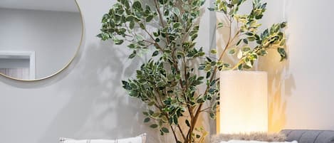 Una sala de estar moderna con un sillón blanco, un sofá gris, un espejo redondo y dos plantas en macetas.
