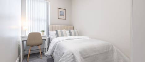A bedroom with a bed, a desk, and a chair.