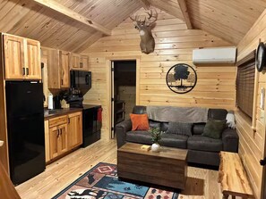 A cabin interior with a kitchen, a living area, and a mounted deer head.