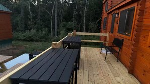 A wooden deck with picnic tables and benches, surrounded by a wooden cabin with windows.