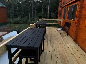 A wooden deck with picnic tables and benches, surrounded by a wooden cabin with windows.