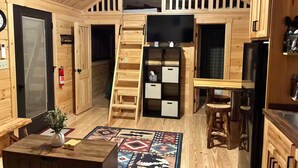 A wooden interior with a loft, a television, a kitchen area, and a patterned rug.