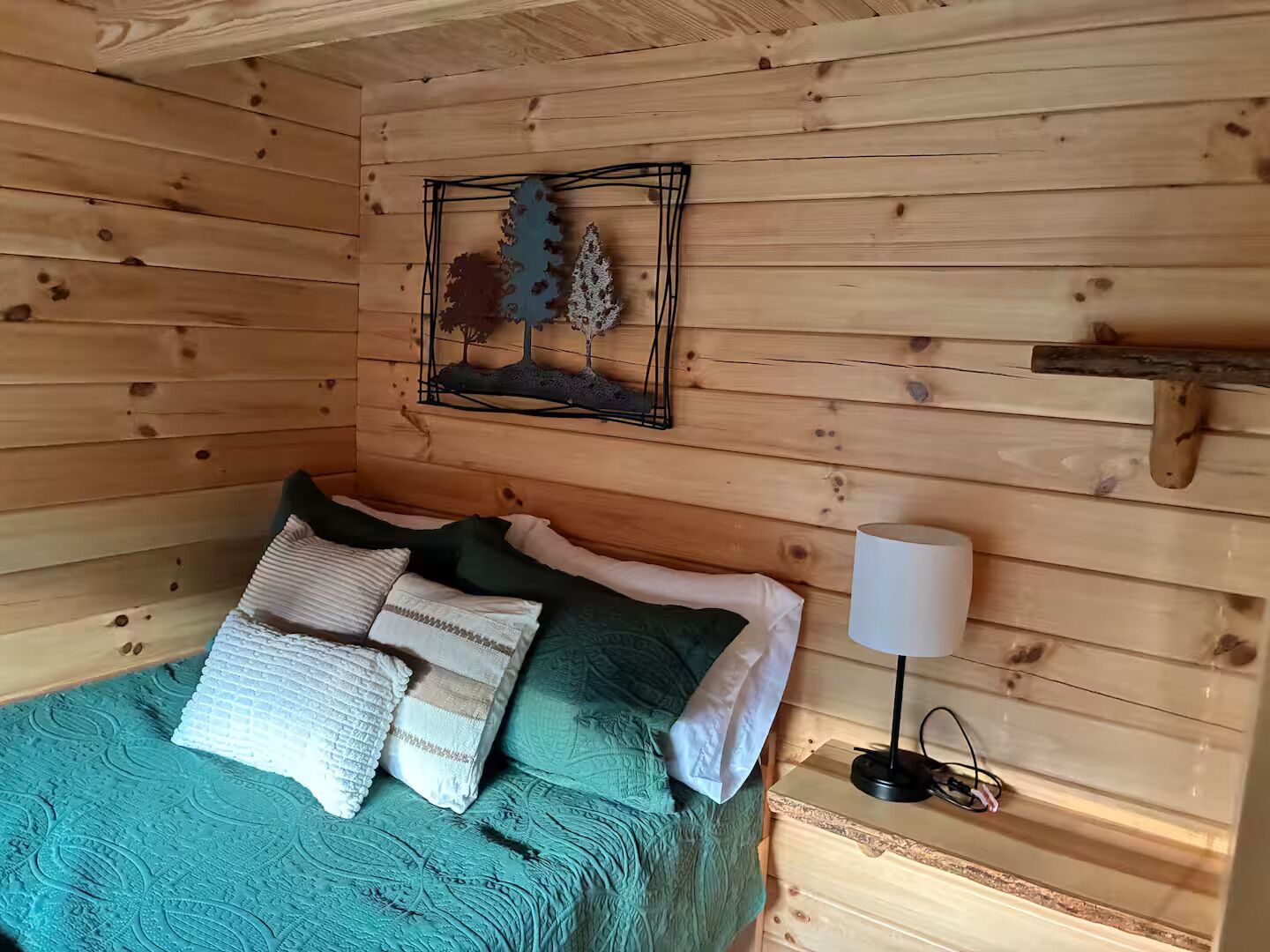 A wooden cabin room with a bed, pillows, a lamp, and a wall decoration.