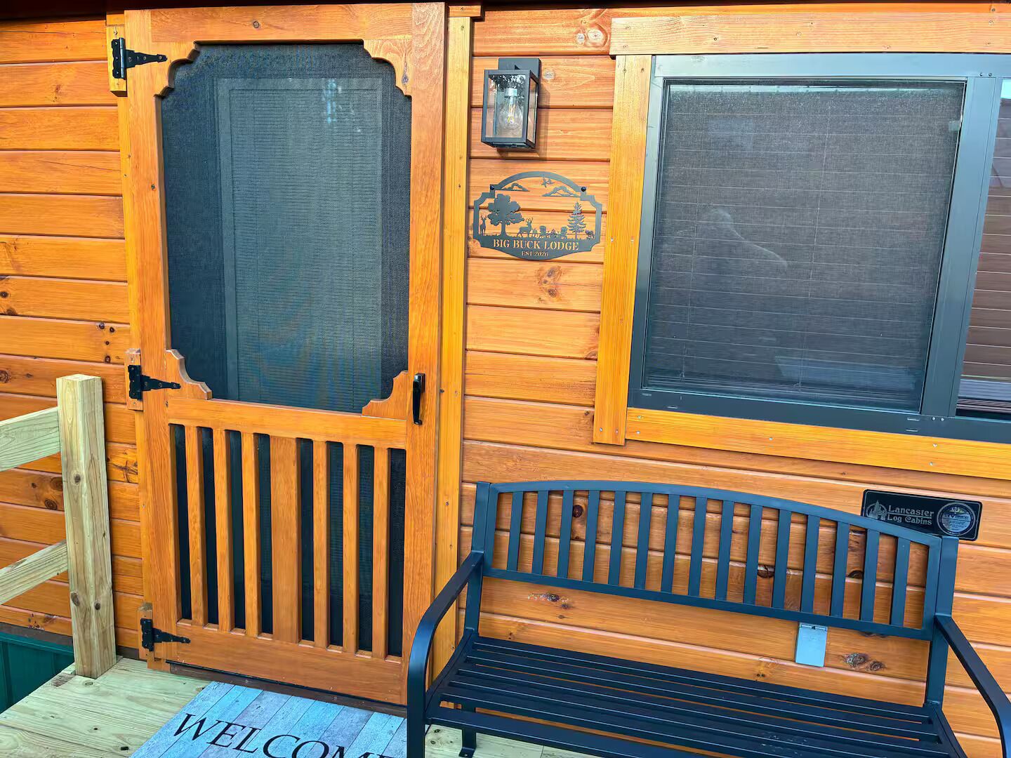 Una cabaña de madera con una puerta, un banco y un felpudo.