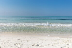 Ein Strand mit klarem türkisblauem Wasser, weißem Sand und sanften Wellen.