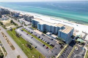 Vue aérienne d’un hôtel avec un parking, situé à côté d’une plage.