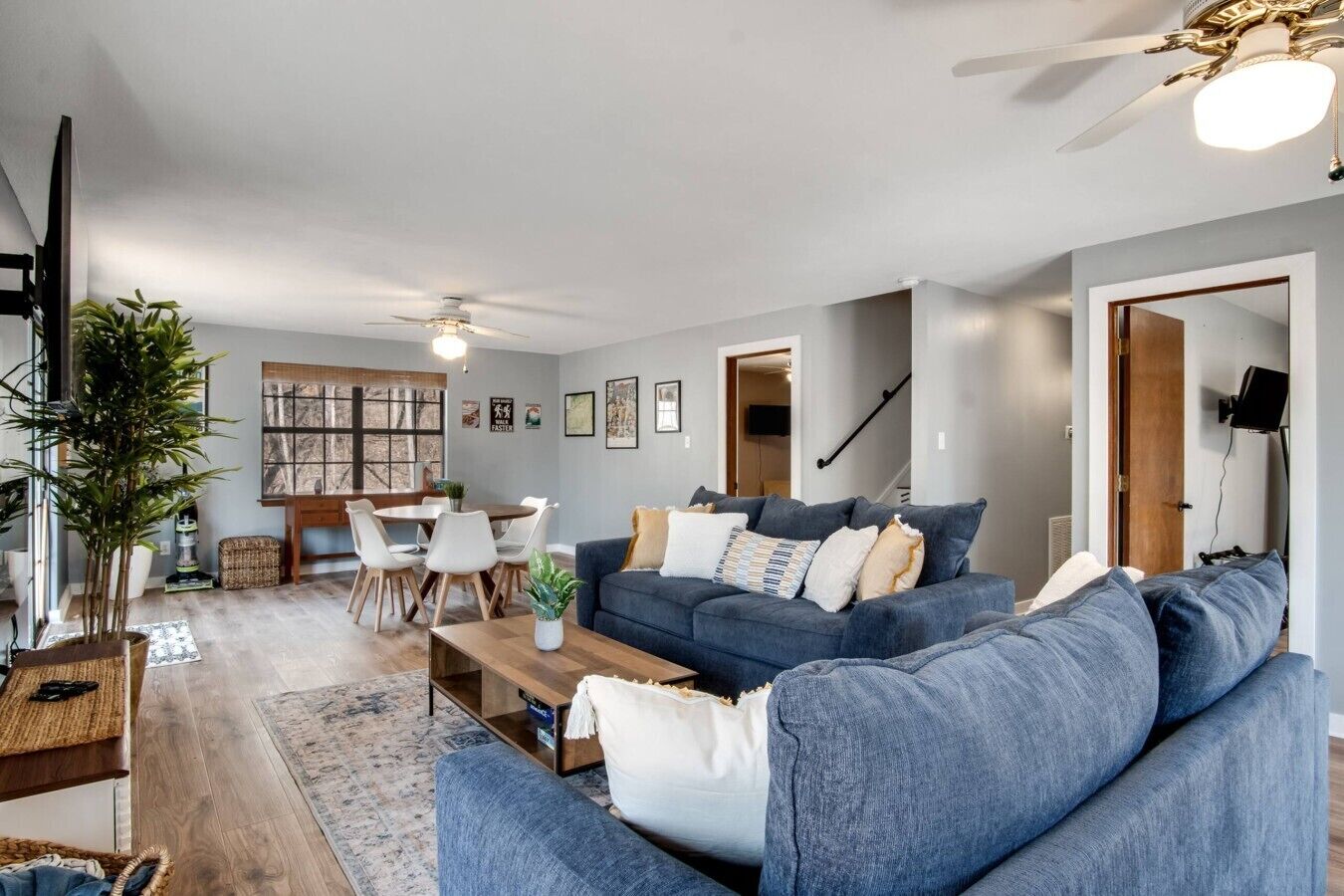 Ein modernes Wohnzimmer mit einem blauen Sofa, einem Esstisch mit Stühlen, einem Deckenventilator und einer Treppe.