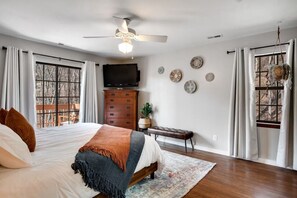 Un dormitorio con una cama grande, ventilador de techo, televisión y vistas al exterior a través de las ventanas.