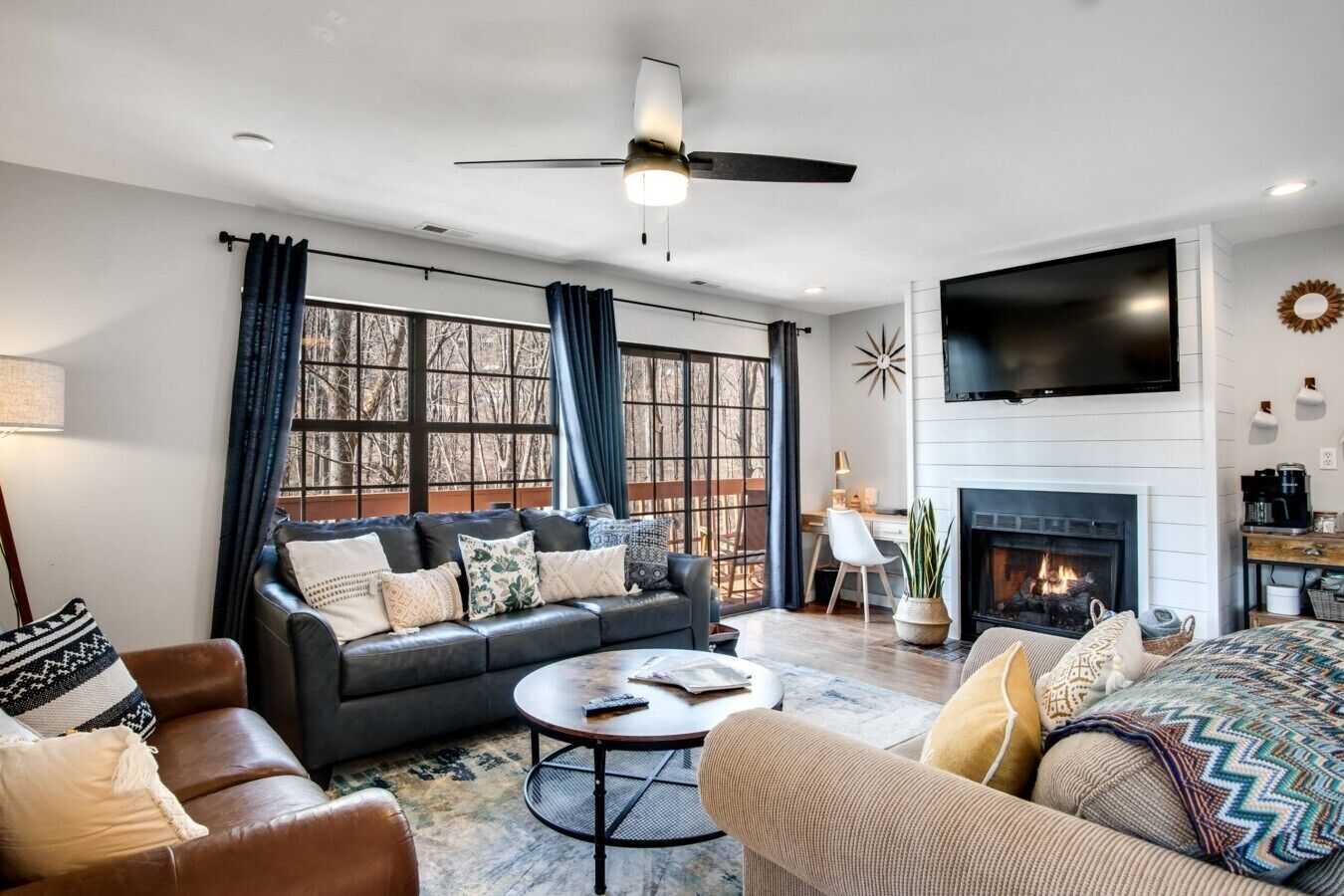 A modern living room with a fireplace, leather sofas, a coffee table, and a flat-screen TV mounted on the wall.