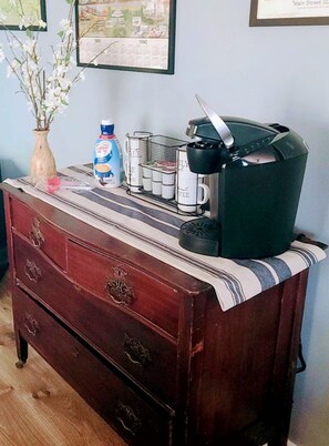 Un aparador de madera con cajones, una cafetera, un florero con flores blancas y un mapa enmarcado en la pared.