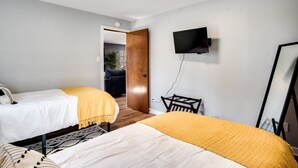 Habitación de hotel con dos camas, un televisor montado en la pared y una puerta que da a otra habitación.