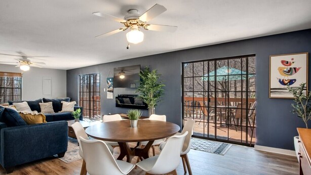 Una sala de estar moderna con una pared gris oscuro, un sofá azul, una mesa de comedor con sillas y un ventilador de techo.