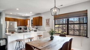 Una cocina moderna con armarios de madera, un refrigerador de acero inoxidable y un comedor con mesa y sillas de madera.