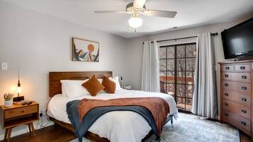 A bedroom with a bed, a nightstand, a dresser, a ceiling fan, a painting, and a window with curtains.