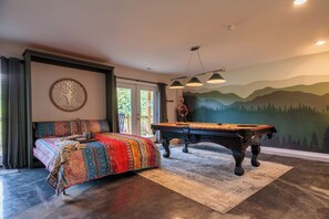 Ein Zimmer mit einem Bett, einem Billardtisch und einem Wandgemälde von Bergen.