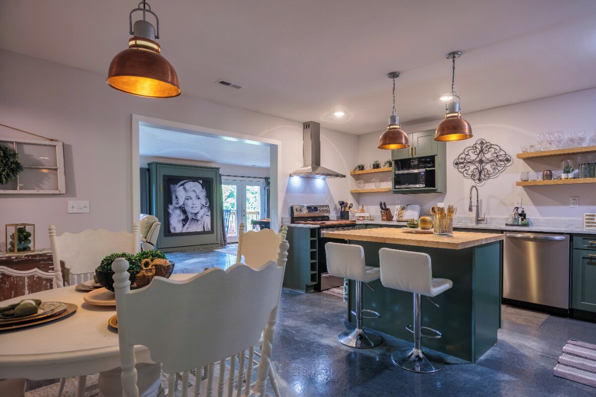 Une cuisine moderne dotée d’un îlot central, de luminaires suspendus et d’un coin repas avec une chaise blanche.