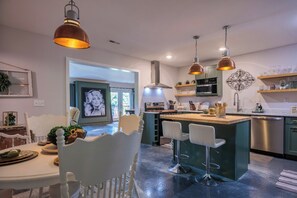 A modern kitchen with a central island, pendant lighting, and a dining area with a white chair. - ⚓ Private Dock Cabin | Pet-Friendly, Hot Tub, Game Room, Arcade, Sleeps 12 Guest (Sevierville)