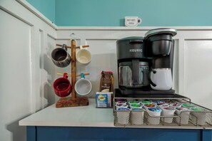 Un ripiano della cucina con una macchina da caffè Keurig, una tazza da caffè, una tazza rossa, una tazza bianca, un portaconfezioni per caffè e una confezione di caffè.