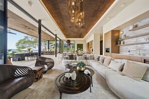 A modern living room with a large sectional sofa, a coffee table, and a dining area with a view. - Exclusive 6BR Ocean-View Villa with detached apartment - Peninsula Papagayo (Peninsula Papagayo, Nacascolo)