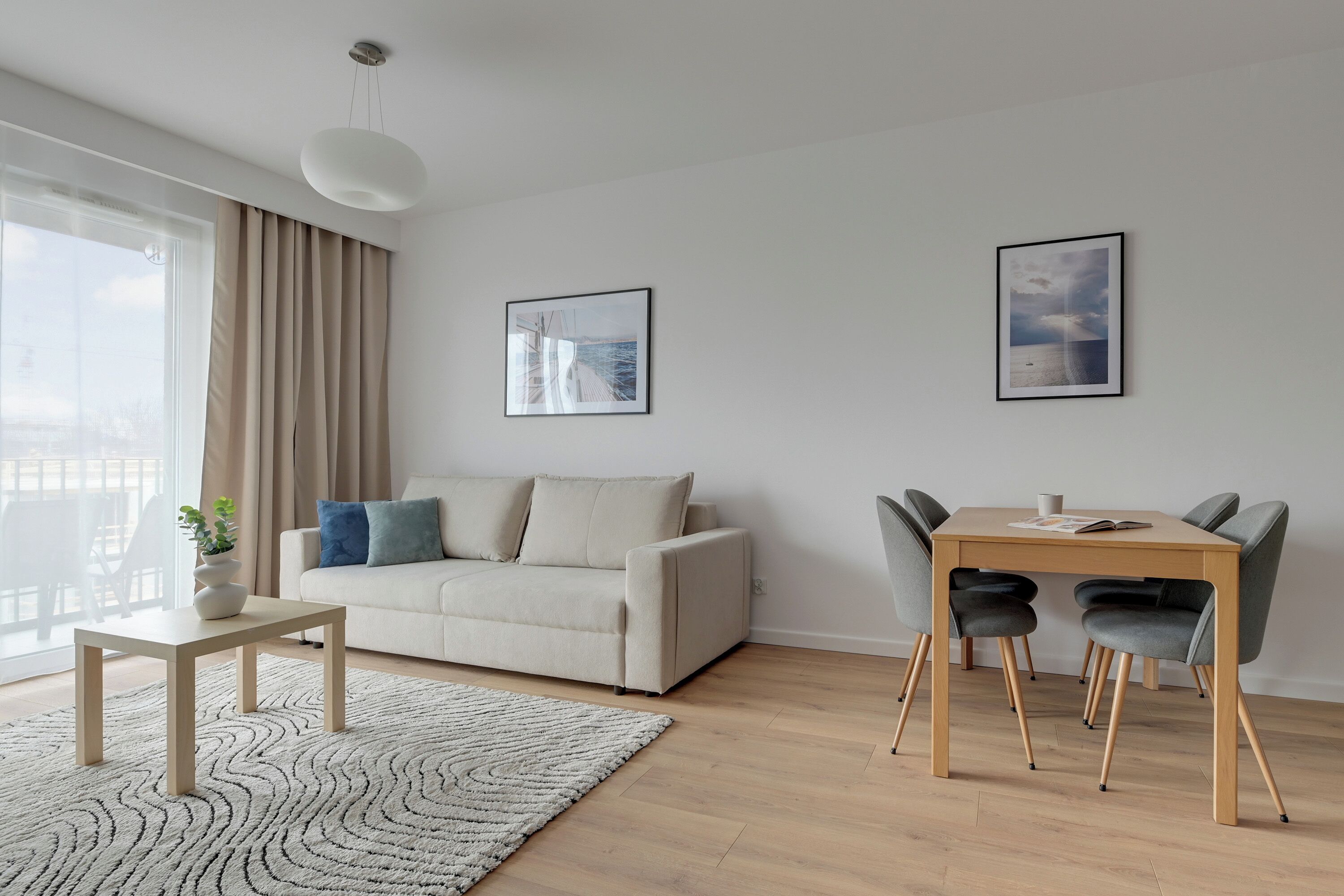 A modern living room with a sofa, a dining table with chairs, a coffee table, a potted plant, and two framed pictures on the wall.