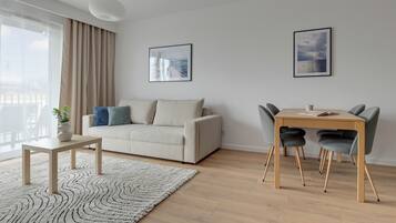A modern living room with a sofa, a dining table with chairs, a coffee table, a potted plant, and two framed pictures on the wall.