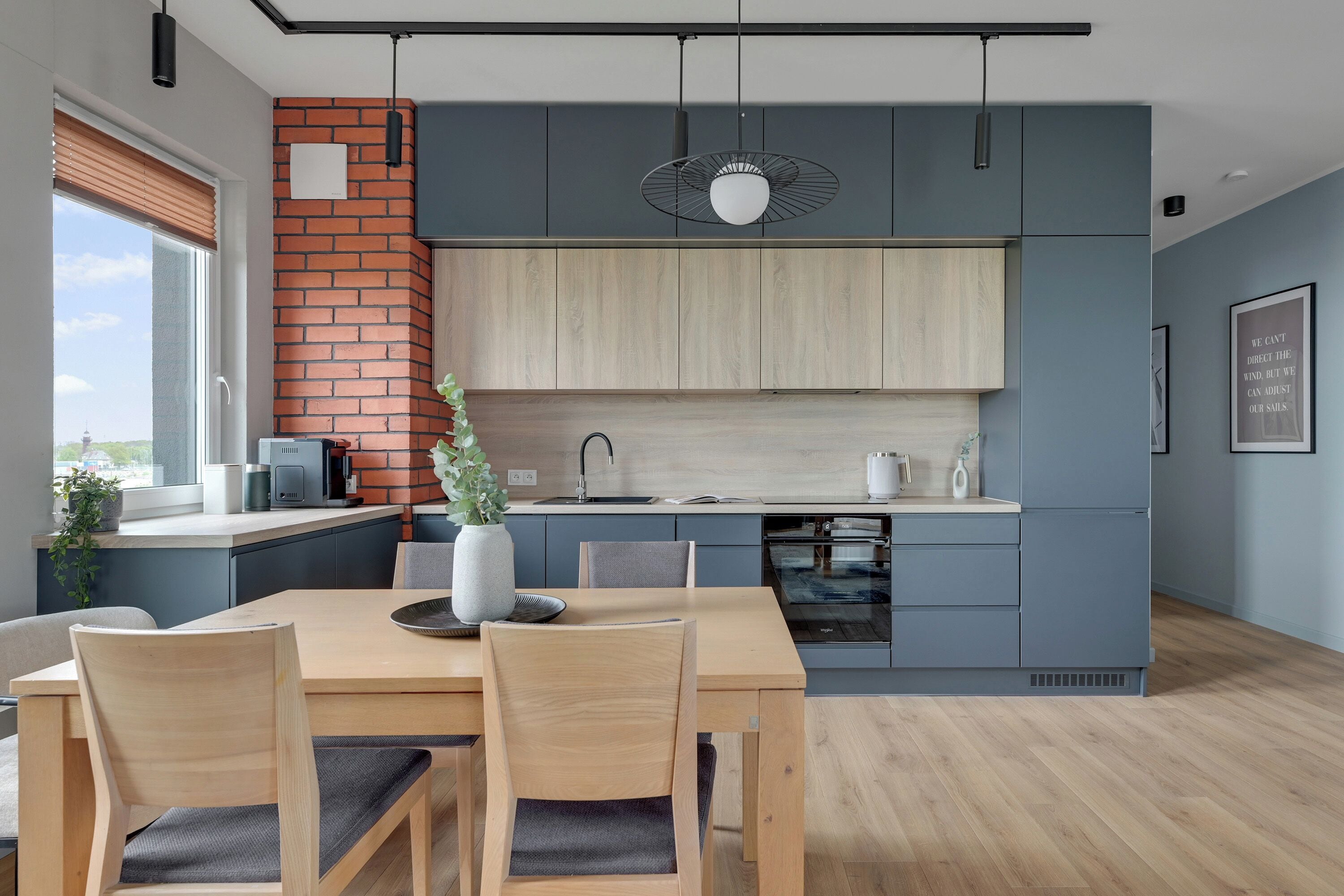 A modern kitchen with a brick accent wall, wooden cabinets, and a dining area with a table and chairs.